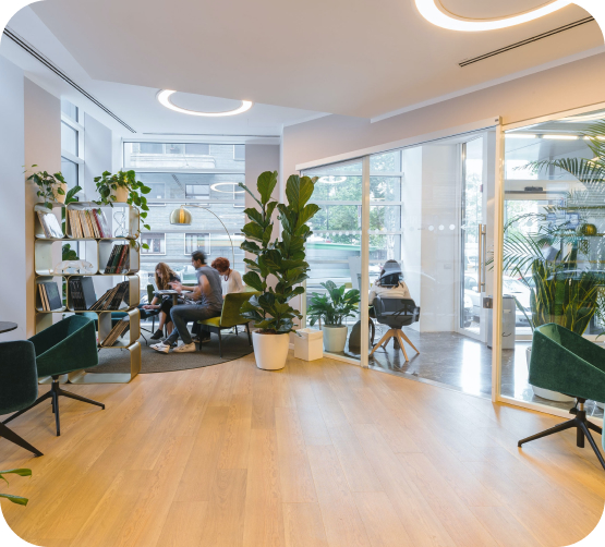 Heller, moderner Büroraum mit Pflanzen, Holzboden und Menschen in Gesprächen an einem Besprechungstisch.